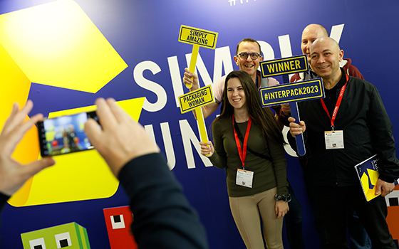 Visitors to interpack smile happily into the camera and hold up signs with the words #interpack, among others. 