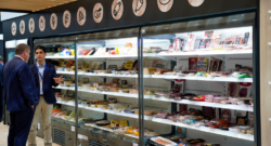 Two men in conversation in front of a refrigerated display case with various packaged foods.